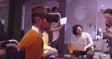 Modern açık uzay ofisinde çalışan engelli bir iş adamı sanal gerçeklik gözlüğü ve İHA simülasyonu kullanarak takım toplantısı yapıyor. Girişim işinde etkin takım çalışması.