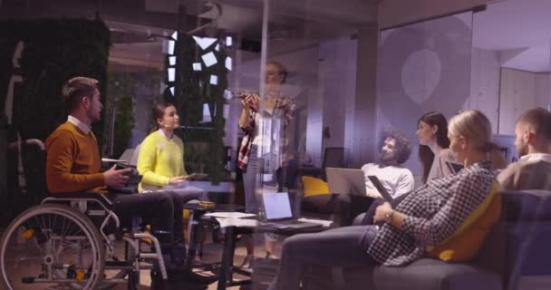 Niepełnosprawny biznesmen na wózku inwalidzkim w pracy w nowoczesnym biurze współpracowników na otwartej przestrzeni na spotkaniu zespołowym z wykorzystaniem gogli wirtualnej rzeczywistości i symulacji dronów. Skuteczna praca zespołowa w biznesie startującym. — Wideo stockowe