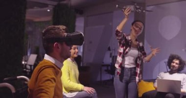 Modern açık uzay ofisinde çalışan engelli bir iş adamı sanal gerçeklik gözlüğü ve İHA simülasyonu kullanarak takım toplantısı yapıyor. Girişim işinde etkin takım çalışması.