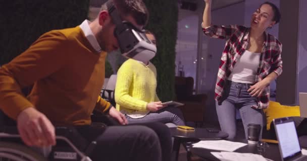Empresario discapacitado en silla de ruedas en el trabajo en la moderna oficina de coworking de espacio abierto en la reunión de equipo utilizando gafas de realidad virtual y simulación de drones. Trabajo en equipo efectivo en una empresa emergente. — Vídeos de Stock