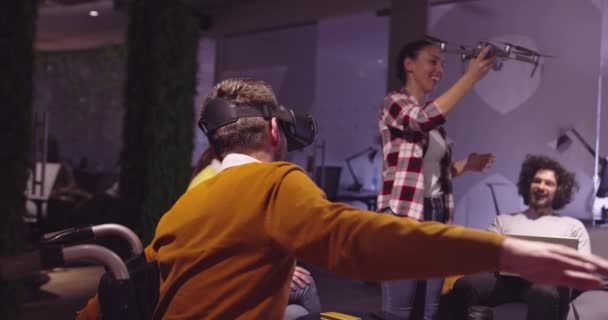 Gehandicapte zakenman in een rolstoel aan het werk in moderne open ruimte coworking office op teamvergadering met behulp van virtual reality bril en drone simulatie. Effectief teamwerk in een startup business. — Stockvideo