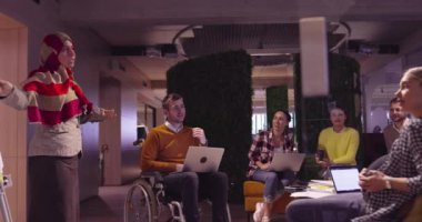 Modern bir açık alanda çalışan Müslüman bir kadın takıma bir sunum yapıyor. Orta Doğulu Arap iş kadını yaratıcı bir ofiste. Ekip toplantısında tekerlekli sandalyedeki engelli iş adamı 