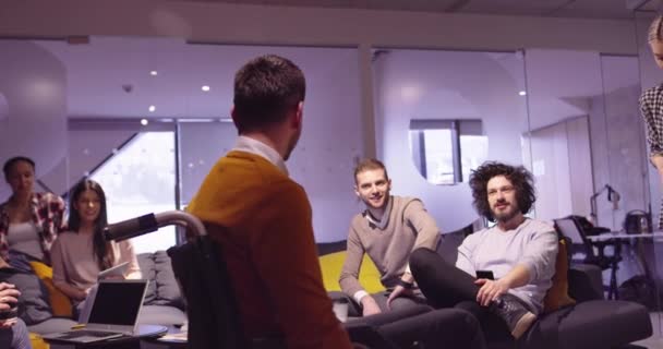 Behinderter Geschäftsmann im Rollstuhl bei der Arbeit in einem modernen Coworking-Büro im offenen Raum bei einem Teammeeting. Effektive Teamarbeit und Einbindung in ein Start-up-Unternehmen. — Stockvideo