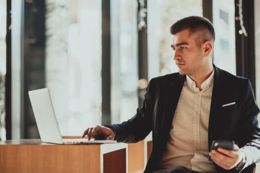 Bir kahve restoranında oturan iş adamı dizüstü bilgisayar ve akıllı telefon üzerinde çalışıyor. Akıllı telefondan mesaj atan iş adamı bilgisayarda çalışıyor ve e-postaları kontrol ediyor.