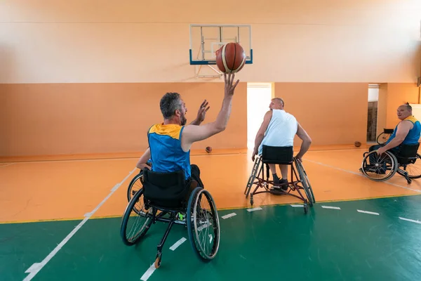 Deficientes veteranos de guerra mista raça e idade equipes de basquete em cadeiras de rodas jogando uma partida de treinamento em um ginásio de esportes salão. Conceito de reabilitação e inclusão de deficientes — Fotografia de Stock