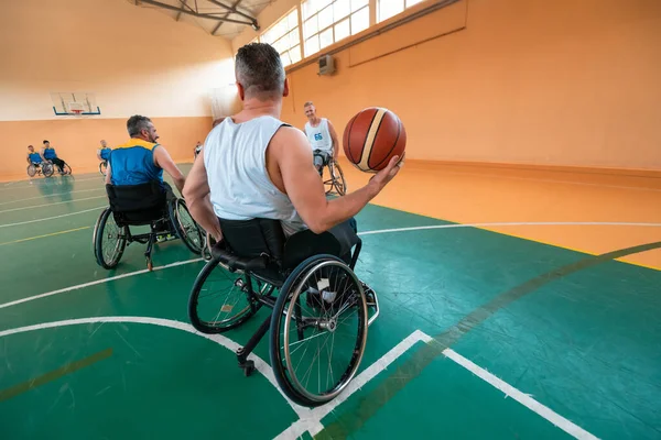 Deficientes veteranos de guerra mista raça e idade equipes de basquete em cadeiras de rodas jogando uma partida de treinamento em um ginásio de esportes salão. Conceito de reabilitação e inclusão de deficientes — Fotografia de Stock