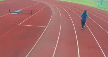 Genç Arap sporcunun tesettürlü atletik vücudu ile stadyum atletizm pistinde koşuşunun sinematik çekimi. Kavram: kararlılık, kadın gücü, hedef başarısı. Yüksek kalite 4k görüntü