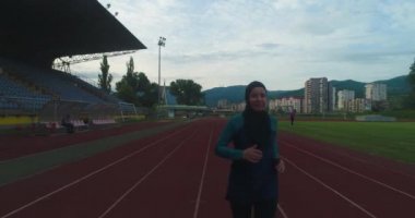 Genç Arap sporcunun tesettürlü atletik vücudu ile stadyum atletizm pistinde koşuşunun sinematik çekimi. Kavram: kararlılık, kadın gücü, hedef başarısı. Yüksek kalite 4k görüntü