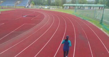 Genç Arap sporcunun tesettürlü atletik vücudu ile stadyum atletizm pistinde koşuşunun sinematik çekimi. Kavram: kararlılık, kadın gücü, hedef başarısı. Yüksek kalite 4k görüntü