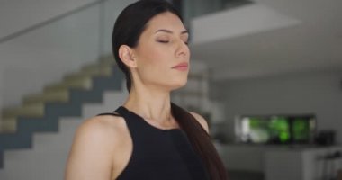 Spor giyim sektöründe karışık bir yarış kadını dizüstü bilgisayarda yoga eğitimi alırken esneme egzersizleri yapıyor. Arka planda kanepe ile oturma odasında egzersiz yapan sağlıklı bir kız..