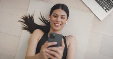 Evde spor yaptıktan sonra akıllı telefon kullanan güzel bir kız. Belirlenmiş Artı Boyut Kadın Fitness İzleyicisi, Yoga Egzersizleri Uygulaması, Çevrimiçi Sağlık Makaleleri Taraması, İnternet 'te Gönderme.