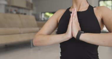 Spor giyim sektöründe karışık bir yarış kadını dizüstü bilgisayarda yoga eğitimi alırken esneme egzersizleri yapıyor. Arka planda kanepe ile oturma odasında egzersiz yapan sağlıklı bir kız..