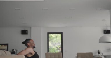 Afro-Amerikan atletik adam dizüstü bilgisayarda online eğitim dersleri izliyor, eğitmenden sonra hareketleri tekrarlıyor, evde bacak egzersizleri yapıyor. Kendini soyutlama. Karantina bölgesi 19.