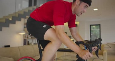 Bisikletli bir adam evde egzersiz yapıyor. Coronavirus Covid19 tecridi sırasında çevrimiçi bisiklet yarışı oynuyor. Yeni normal konsept. Yüksek kalite 8K görüntü