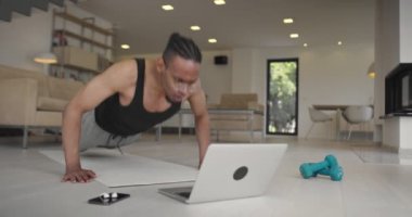 Sıkı çalışma. Bitkin bir adam. Zayıf eller. Online eğitim. Evde spor salonu. Afro-Amerikan yorgun adam yumruklarıyla şınav çekiyor dizüstü bilgisayarla yoga minderinin ışığından düşerek iç tarafa bakıyor. Yüksek