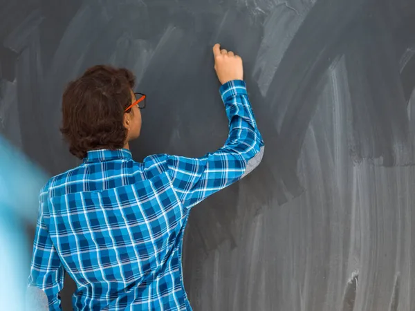 Intelligente arabo teen ragazzo con gesso in mano scrittura su vuoto nero bordo in scuola — Foto Stock