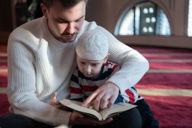 Müslüman dua eden baba ve oğul camide dua ediyor ve kutsal kitap Kuran 'ı birlikte okuyorlar. İslam eğitimi kavramı.