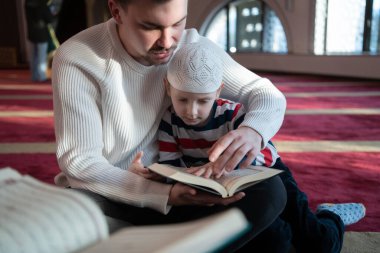 Müslüman dua eden baba ve oğul camide dua ediyor ve kutsal kitap Kuran 'ı birlikte okuyorlar. İslam eğitimi kavramı.