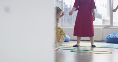 Küçük anaokulu öğrencileri ve bayan öğretmenleri sınıfın içinde egzersiz yapıyorlar. Hula hoop pistinin üzerinden zıplıyordu. Yüksek kalite 4k görüntü