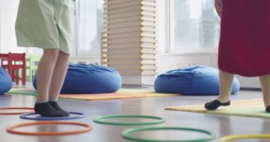 Küçük anaokulu öğrencileri ve bayan öğretmenleri sınıfın içinde egzersiz yapıyorlar. Hula hoop pistinin üzerinden zıplıyordu. Yüksek kalite 4k görüntü