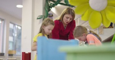 Bir kreşteki sanat dersinde yaratıcı çocuklar ya da ilkokul sınıfında bayan öğretmenle resim çizen çocuklar. Ağır çekim. Yüksek kalite 4k görüntü