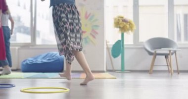 Küçük anaokulu öğrencileri ve bayan öğretmenleri sınıfın içinde egzersiz yapıyorlar. Hula hoop pistinin üzerinden zıplıyordu. Yüksek kalite 4k görüntü