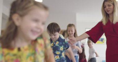Küçük anaokulu öğrencileri ve bayan öğretmenleri sınıfın içinde egzersiz yapıyorlar. Hula hoop pistinin üzerinden zıplıyordu. Yüksek kalite 4k görüntü