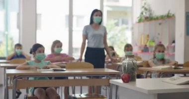 Okulda yüz maskesi takan bayan öğretmen, okulda çocuklara öğretmenlik yapıyor. Eğitim, Covid19 Coronavirus salgını sırasında sağlık güvenliğine geri döndü.