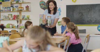 İlkokulda biyoloji sınıfında çocuklu bir bayan öğretmen biyoloji ya da sürdürülebilir bitkilerle ilgili botanik bilimsel deney yapıyor. Bitkileri bir bardakta öğrenmek.