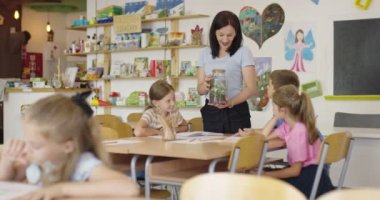 İlkokulda biyoloji sınıfında çocuklu bir bayan öğretmen biyoloji ya da sürdürülebilir bitkilerle ilgili botanik bilimsel deney yapıyor. Bitkileri bir bardakta öğrenmek.