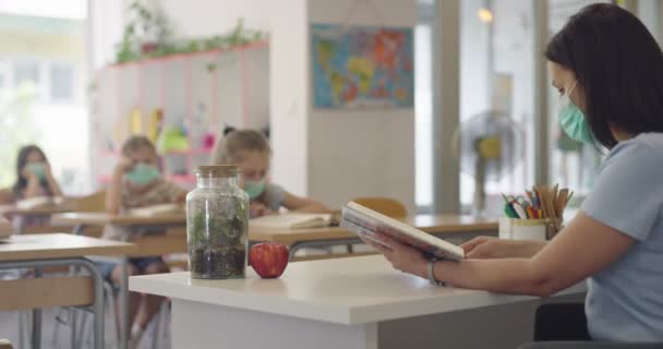 In der Schule sitzen maskierte Kinder im Klassenzimmer und hören dem Lehrer zu. Unterricht während der Pandemie in der Schule. — Stockvideo