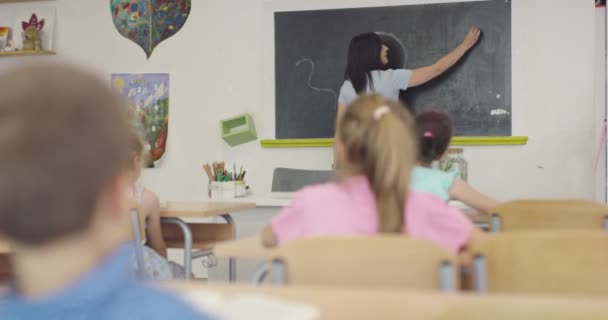 Lärande i skolan, kvinnlig lärare skriver med krita på tavlan. — Stockvideo