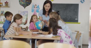 Coğrafya sınıfındaki coğrafya öğretmeni. Bir grup mutlu okul öğrencisinin yan görüntüsü. Okuldaki sınıflarında küre olan çocuklar..