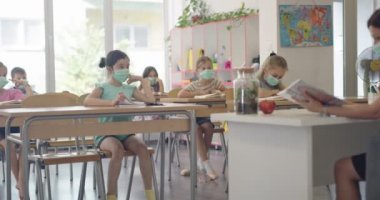 Sınıftaki maskeli çocuklar sınıfta oturur ve öğretmenlerini dinlerler. Okulda salgın sırasında alınan dersler.