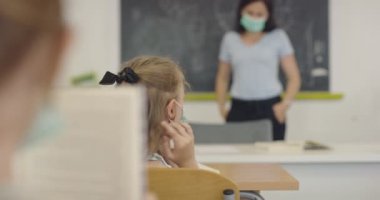 Öğretmen çocuk öğrenciyle yüzüne maske takması için konuşuyor. Okulda salgın sırasında alınan dersler.