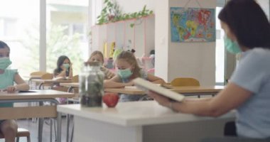 Sınıftaki maskeli çocuklar sınıfta oturur ve öğretmenlerini dinlerler. Okulda salgın sırasında alınan dersler.