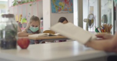 Sınıftaki maskeli çocuklar sınıfta oturur ve öğretmenlerini dinlerler. Okulda salgın sırasında alınan dersler.