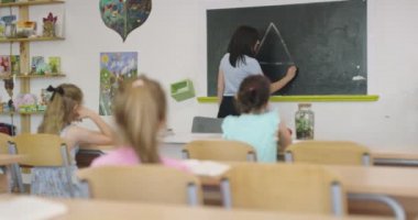 Bayan öğretmen okulda öğrenme sürecini tahtaya tebeşirle yazıyor..