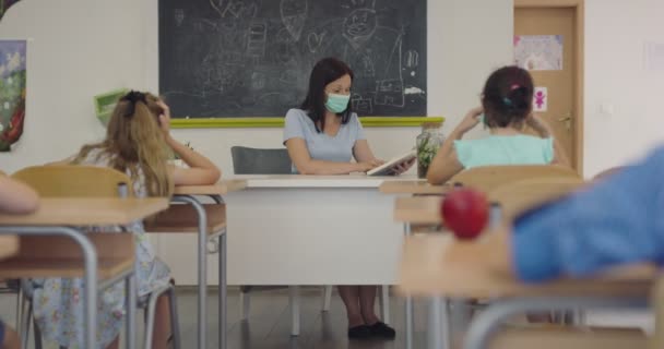 Vrouwelijke leraar draagt gezichtsmasker op school, geeft les aan kinderen op school. Onderwijs terug naar de veiligheid op school tijdens de Covid19 Coronavirus pandemie. — Stockvideo