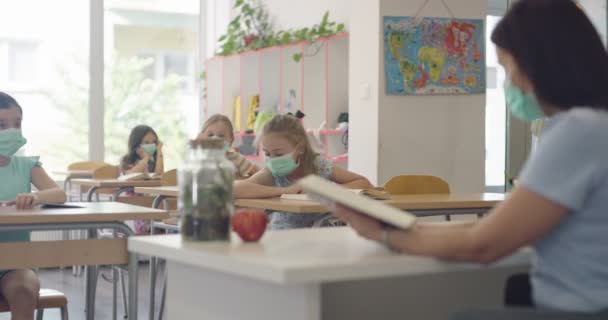 仮面の学校の教室の子供たちは教室に座って先生の言うことを聞いています。学校でのパンデミック時の教訓. — ストック動画