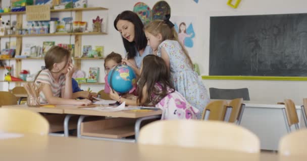 Professora com crianças na aula de geografia a olhar para o globo. Vista lateral do grupo de crianças diversas da escola feliz com globo na sala de aula na escola. — Vídeo de Stock