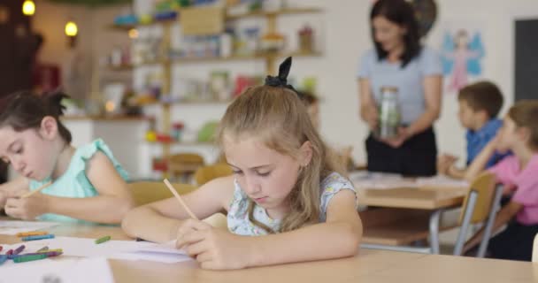 Niños pintando en la sala de juegos. Dos niñas dibujando sobre papel en la mesa en el aula. — Vídeos de Stock