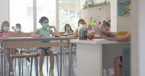Діти в класі в школі в масках сидять в класі і слухають вчителя. Уроки під час пандемії в школі . — стокове відео