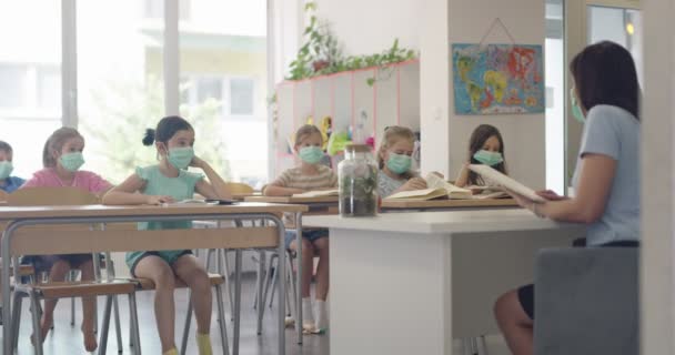 Los niños en el aula en la escuela con máscaras se sientan en el aula y escuchan al maestro. Lecciones durante la pandemia en la escuela. — Vídeos de Stock