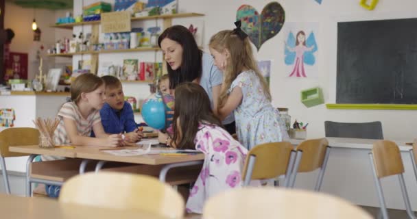 Insegnante di sesso femminile con bambini in geografia classe guardando globo. Vista laterale di gruppo di diversi bambini della scuola felice con globo in classe a scuola. — Video Stock