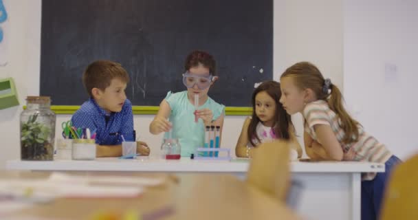 Általános Iskolai Tudomány Tanterem: Lelkes tanár elmagyarázza a kémiát a gyermekek különböző csoportjának, a kisfiú keveri a vegyi anyagokat a főzőpoharakban. A gyermekek érdeklődéssel tanulnak — Stock videók