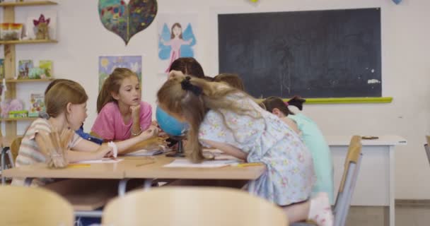 Insegnante di sesso femminile con bambini in geografia classe guardando globo. Vista laterale di gruppo di diversi bambini della scuola felice con globo in classe a scuola. — Video Stock
