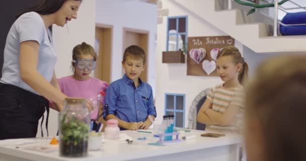 Basisschool Science Classroom: Enthousiaste leraar legt scheikunde uit aan diverse groep kinderen, Little Boy Mixes Chemicals in Beakers. Kinderen leren met rente — Stockvideo