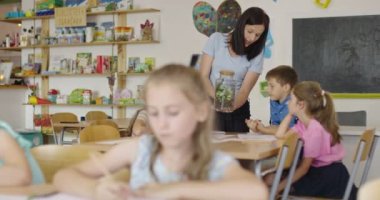 İlkokulda biyoloji sınıfında çocuklu bir bayan öğretmen biyoloji ya da sürdürülebilir bitkilerle ilgili botanik bilimsel deney yapıyor. Bitkileri bir bardakta öğrenmek.