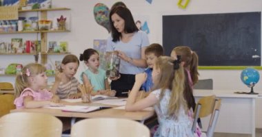 İlkokulda biyoloji sınıfında çocuklu bir bayan öğretmen biyoloji ya da sürdürülebilir bitkilerle ilgili botanik bilimsel deney yapıyor. Bitkileri bir bardakta öğrenmek.